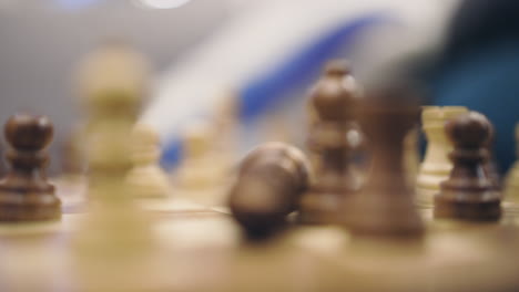 close-up of male fingers making chess king fall over on wooden board