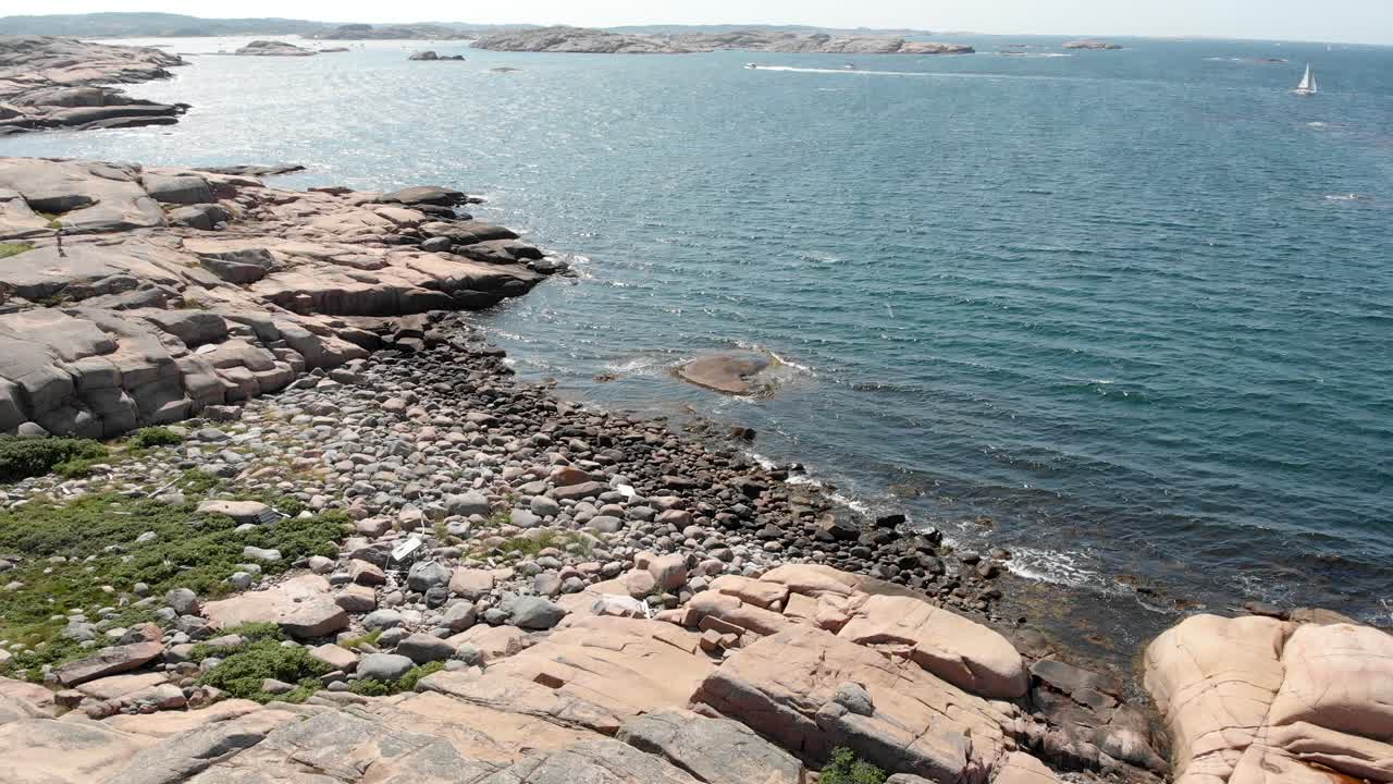 Aerial pull out shot capturing the unspoiled calm shimmering blue sea and barren rocks against the open horizon in summer, Bohuslan coast, Sweden
