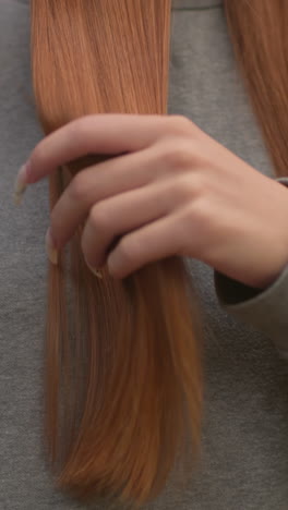 primer plano de una mujer joven cepillando su cabello liso y marrón rojizo con un cepillo de pelo rosa contra su suéter gris en un entorno de bosque sereno