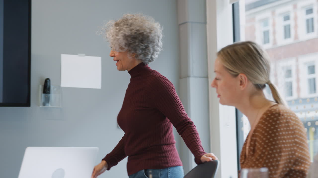 성숙한 사업가 여성은 현대적인 사무실에서 테이블 주위에 협력하는 여성들의 창의적인 회의를 이끌고 있습니다.