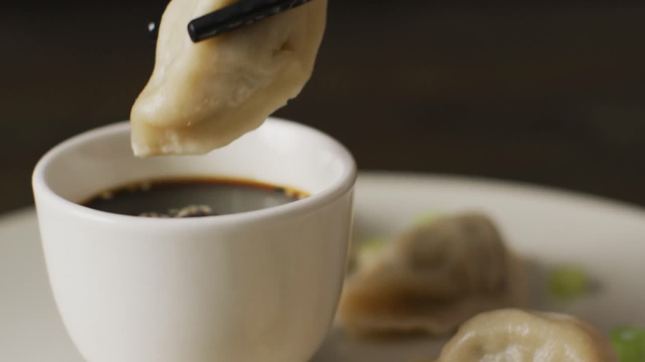 Chopsticks with gyoza dumpling and soy sauce on black background