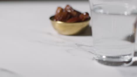 close up of bowl of dates and glass of water on marble surface celebrating muslim festival of eid