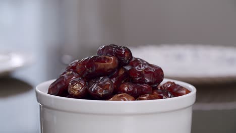 arab woman in traditional abaya dress placing ripe dates in a white bowl on top of table