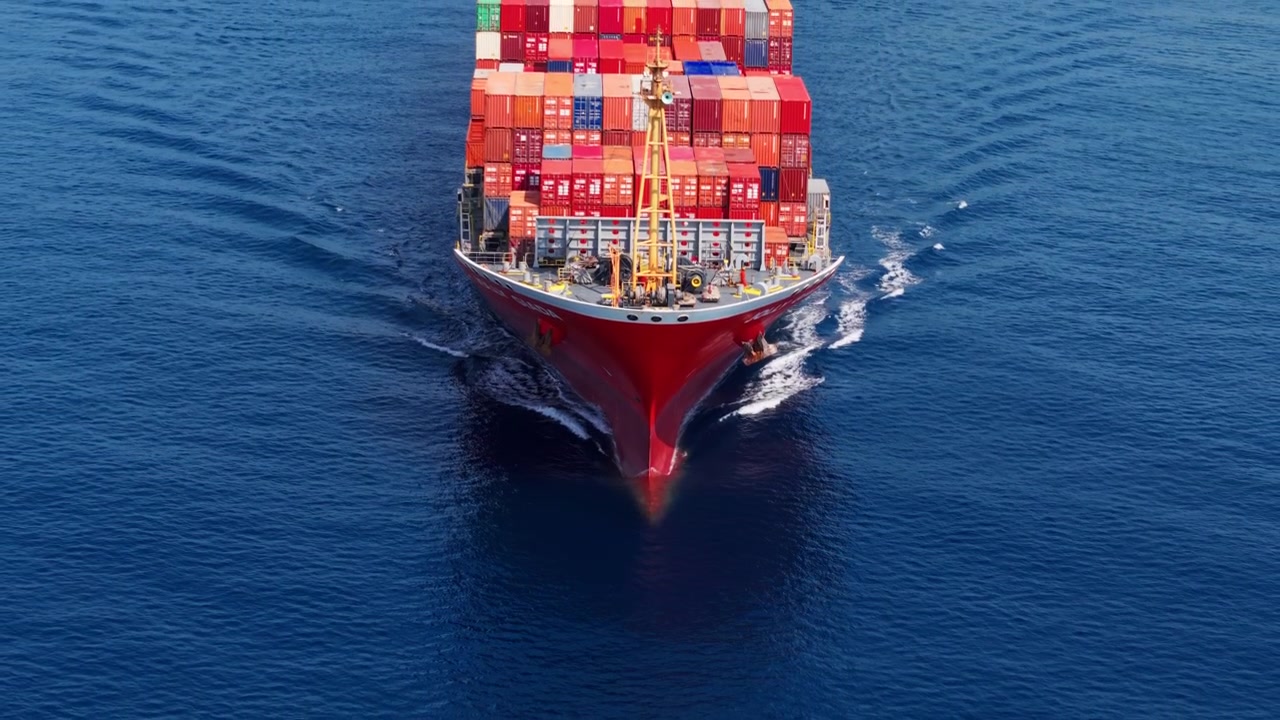 Large cargo ship loaded with containers moves steadily through calm blue sea waters