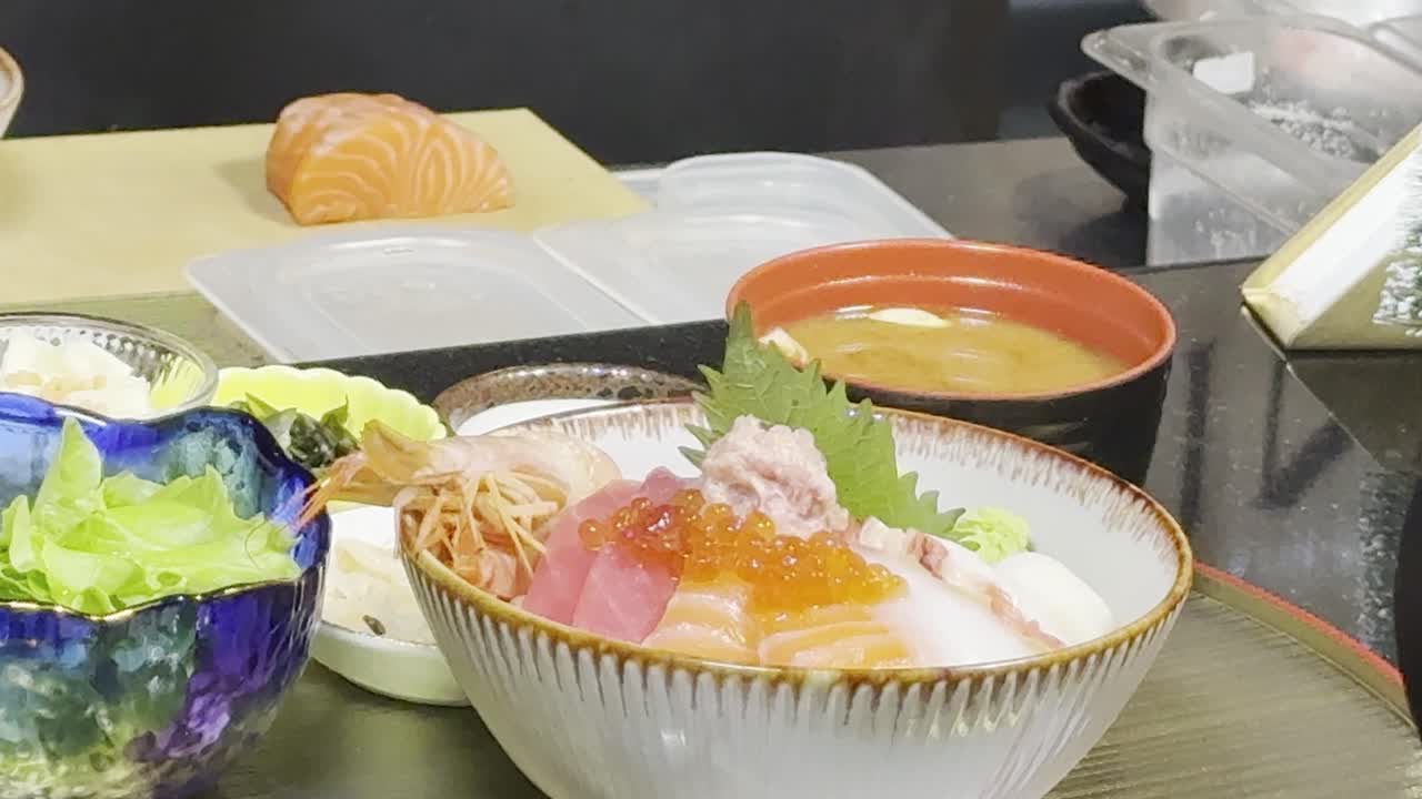 Static close-up of colorful sashimi rice bowl with salad and soup under bright restaurant lighting