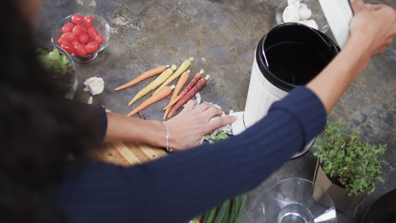 mujer biracial compostando residuos de verduras en la cocina, cámara lenta