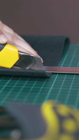 cu: person cuts black leather fabric with special box cutter near metal ruler on mat board close view