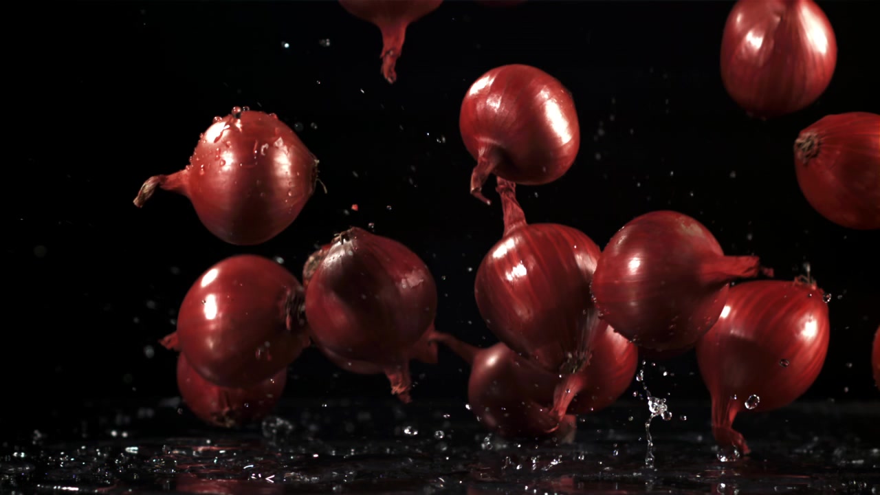Rødløg falder i slowmotion med vandsprøjt på sort baggrund