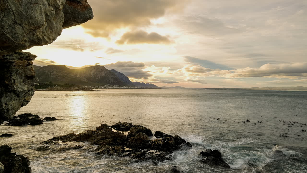 Timelapse from coastal cliffs over ocean of vivid golden sunrise behind mountain