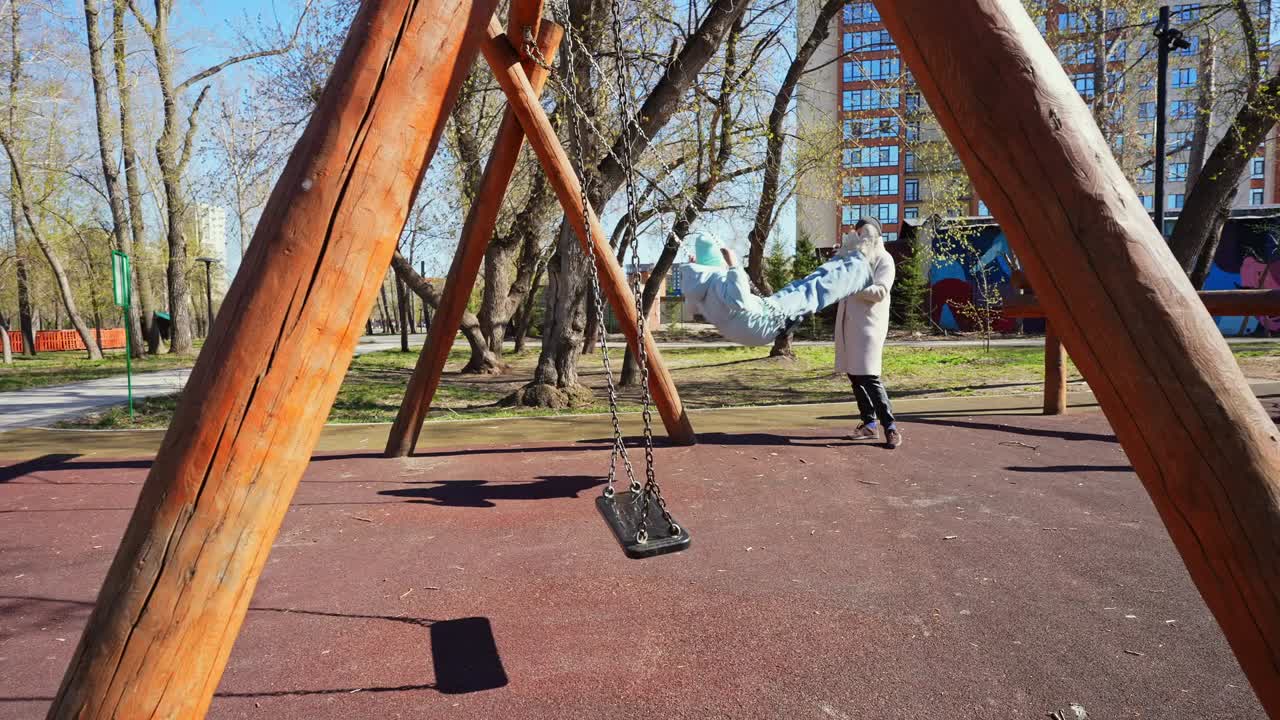 Donna sull'altalena al parco giochi mentre un amico la riprende con il telefono.