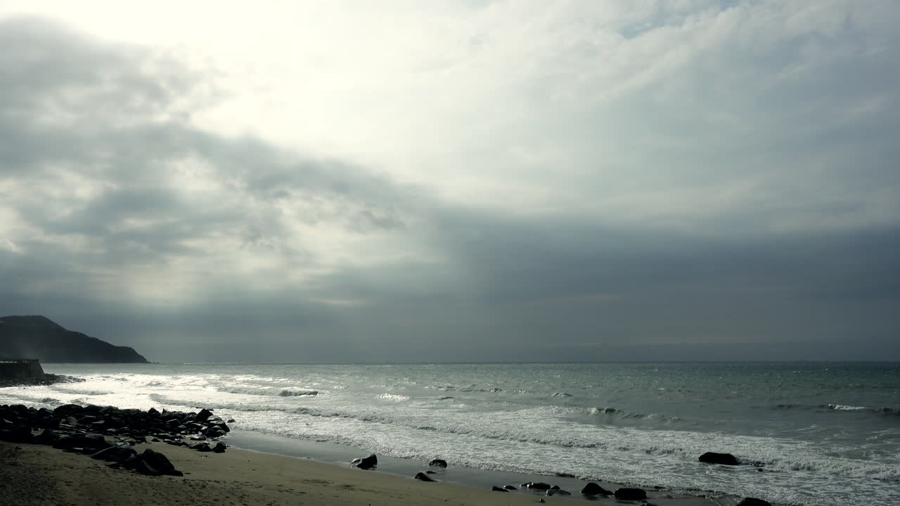 Beach shoreline with rocks and sand at Fukuoka Sea Shrine with cloudy daytime sky wide shot