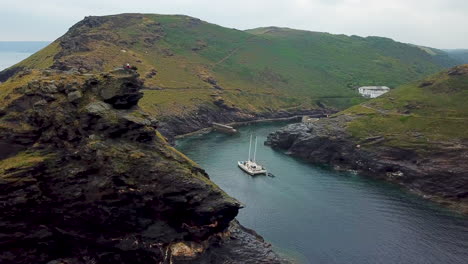 Boat-on-Cornwall-coastline,-entering-fishing-port-harbour-inlet,-UK,-aerial