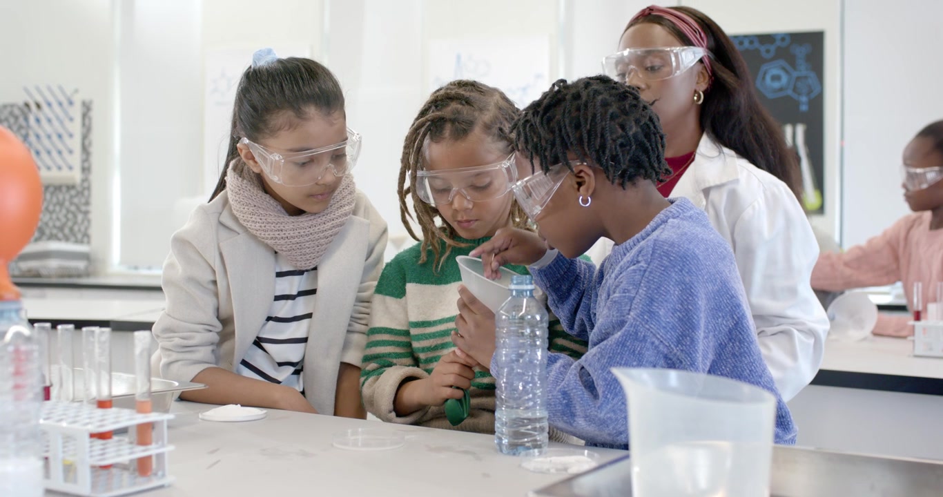 Diverse children after teacher cue conducting funnel demo at lab bench, stirring to inflate balloon