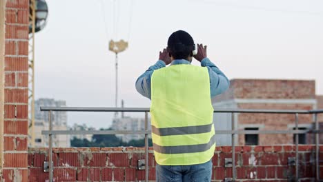 rear of the african american man architect or foreman in vr glasses standing on the roof at the building site and having headset as watching virtual tour of future architecture. outside. new modern technologies. back view.