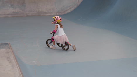 young girl learning to ride balance bike in skatepark