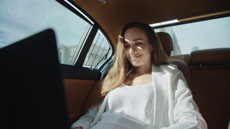 Smiling-business-woman-getting-good-news-on-laptop-in-car.-Ceo-reading-project