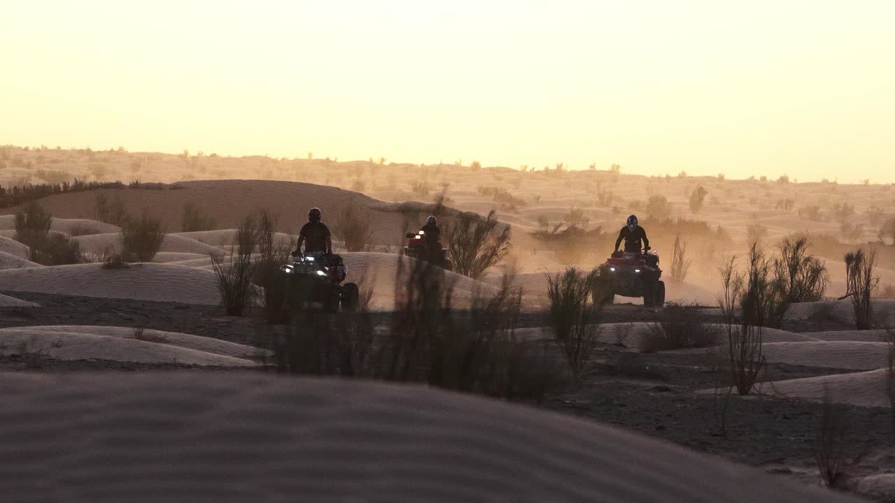 Gruppo di quad che attraversano il deserto tunisino al tramonto, sollevando polvere tra le dune con luce dorata, cespugli secchi e atmosfere avventurose nel selvaggio paesaggio arido del Nord Africa