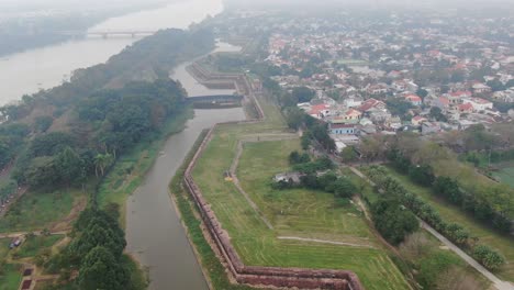 Vista-Aérea-De-Drones-En-Vietnam-Volando-Sobre-Jardines-Verdes,-Templos,-Canales-Y-Pequeños-Edificios-En-Un-Día-Nublado-Y-Brumoso