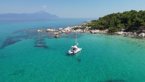 Katamaranboot-Und-Menschen-Schwimmen-In-Der-Türkisblauen-Bucht-In-Chalkidiki,-Griechenland---4K-Luftaufnahme