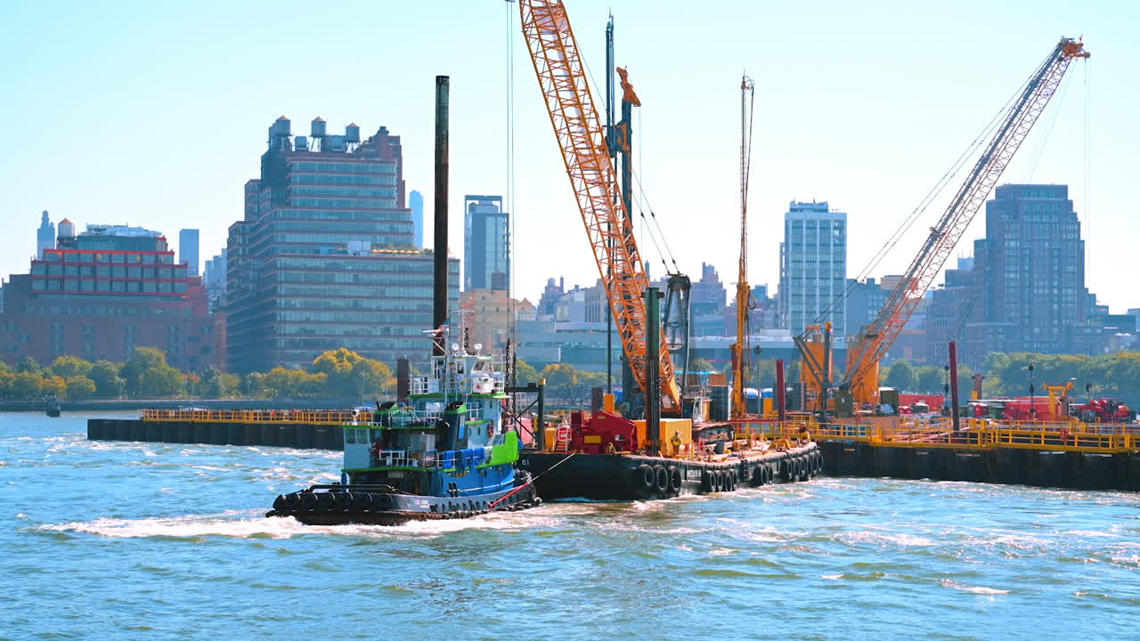 New York, USA, 9 August 2025: Tugboat and construction site on Hudson River in New York. A tugboat operates near a construction barge on the Hudson River with Manhattan buildings in the background