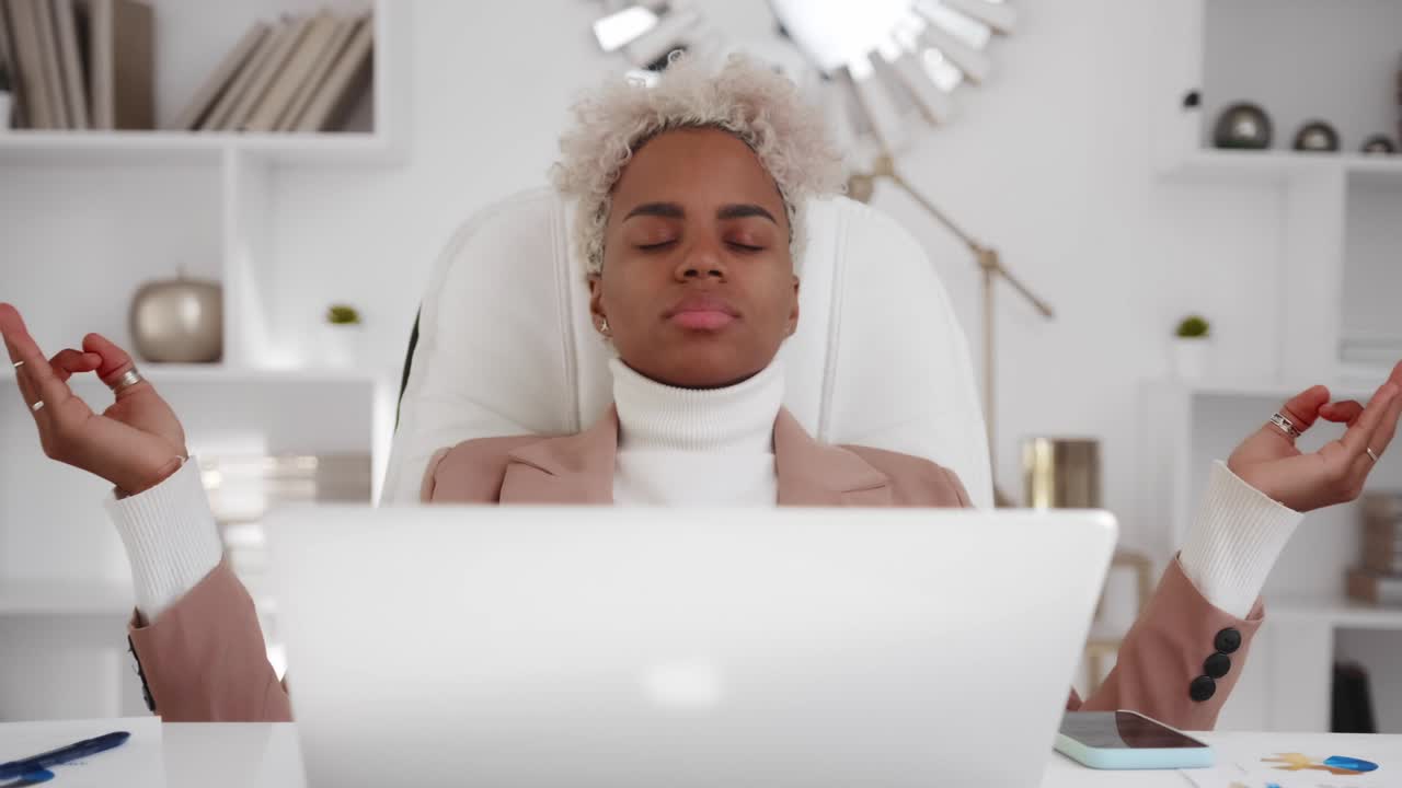 Giovane donna d'affari afroamericana che medita e pratica yoga per alleviare lo stress.