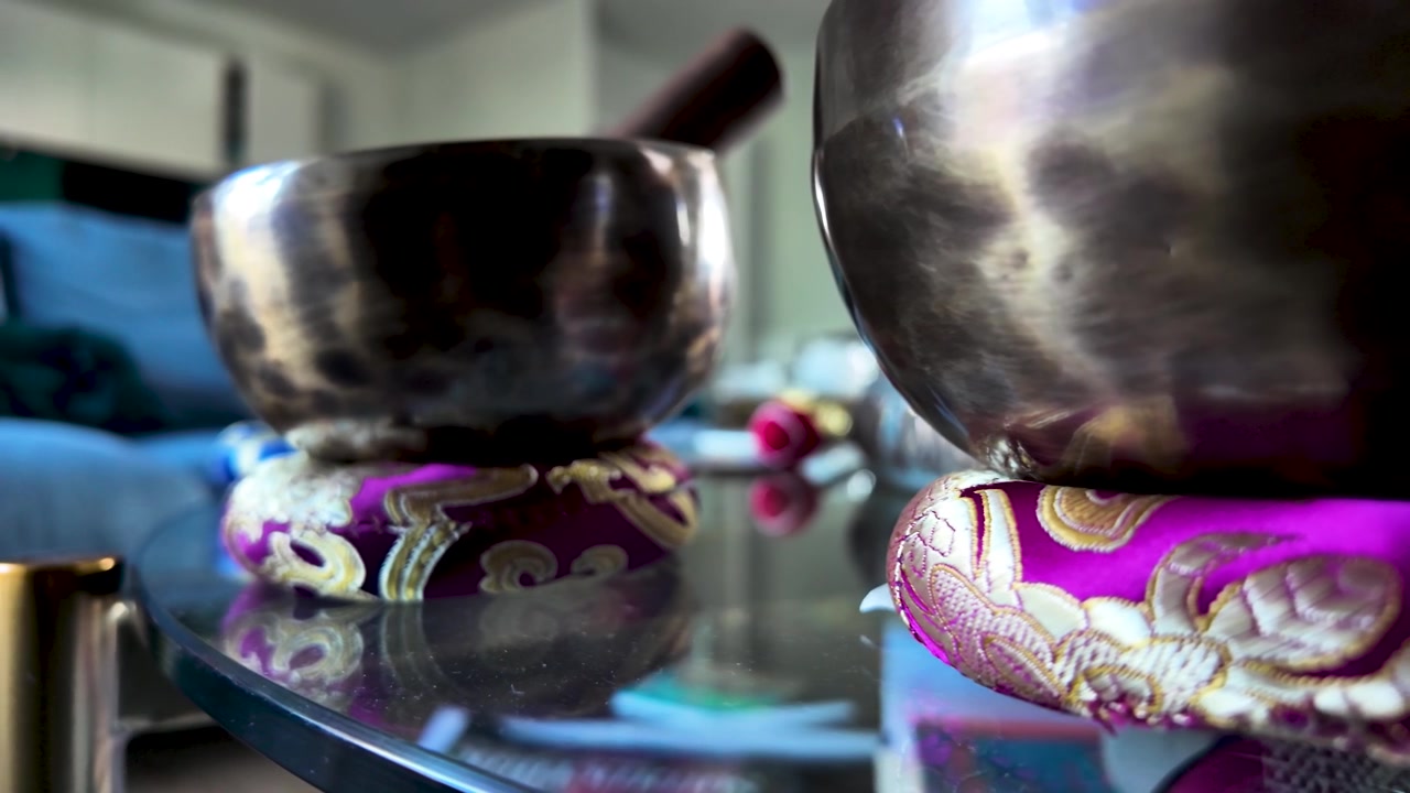Two singing bowls sit on colorful cushions, reflecting on a glass table. Ideal for meditation and relaxation content. close up shot