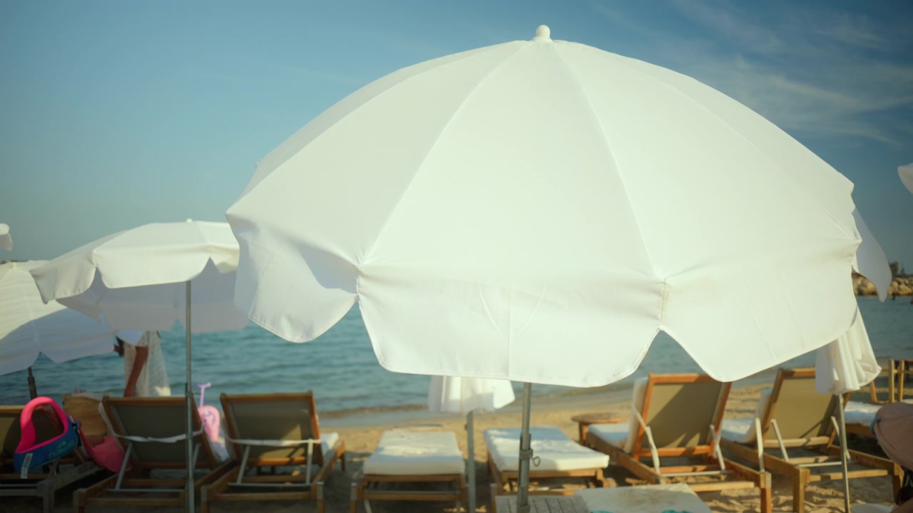 Ombrellone da spiaggia bianco in una giornata di sole che offre ombra, con sedie a sdraio e l'oceano sullo sfondo, creando una rilassante scena estiva.