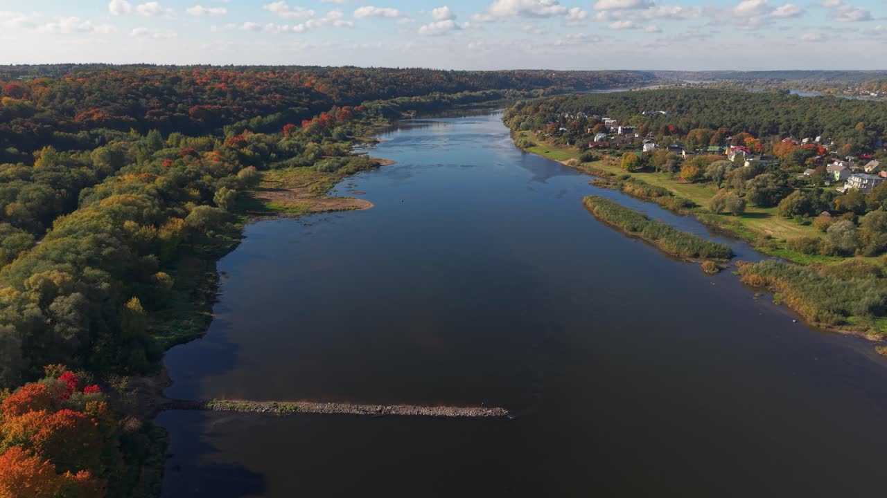 Aerial view of the Nemunas River flowing near Kaunas, Lithuania, with vibrant autumn trees and countryside homes lining the riverbanks on a bright and clear day