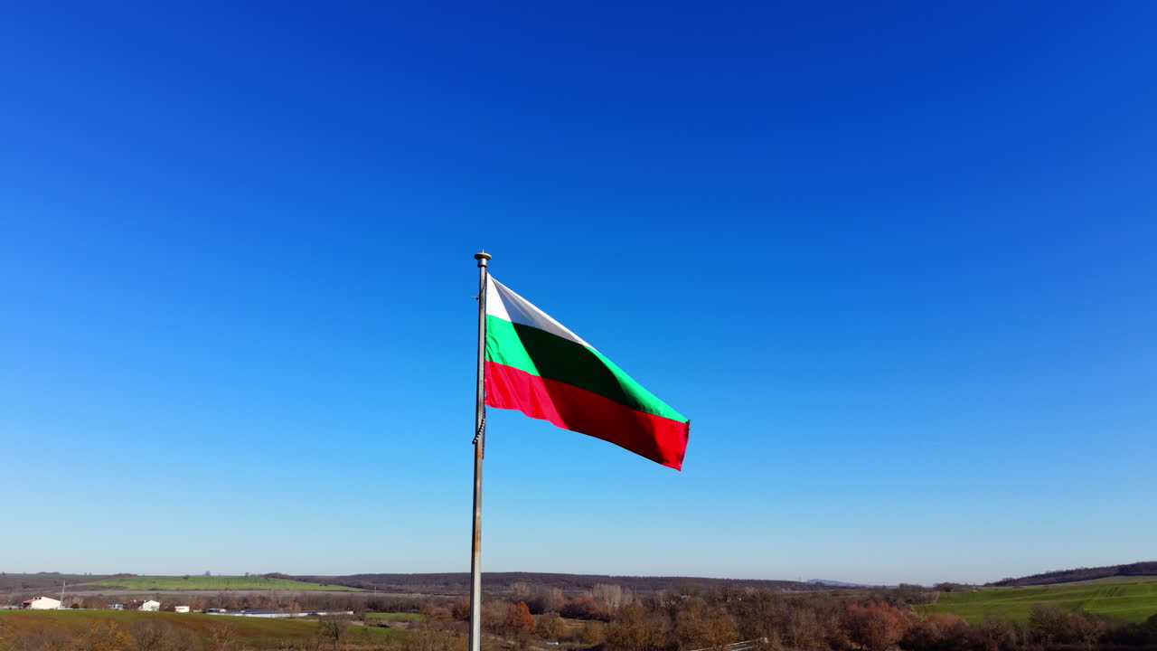 Bandiera bulgara bianca, verde e rossa su un'asta di metallo con sfondo paesaggistico. Bandiera nazionale della Bulgaria che sventola contro un cielo azzurro limpido. Vista aerea.
