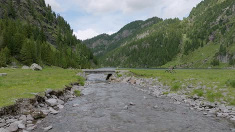 Wide-shot-of-cyclist-with-mtb-stopping-on-bridge-and-watching-beautiful-lake-with-mountains