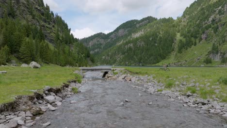 wide shot of cyclist with mtb stopping on bridge and watching beautiful lake with mountains