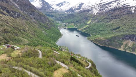 geiranger fjord and village seen from above ornevegen eagles road - aerial during spring with lush hillsides and snow capped mountain peaks