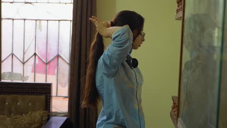 A-pretty-Asian-young-girl-with-glasses-and-headphones-on-her-neck-tying-her-ponytail-while-standing-in-front-of-the-mirror