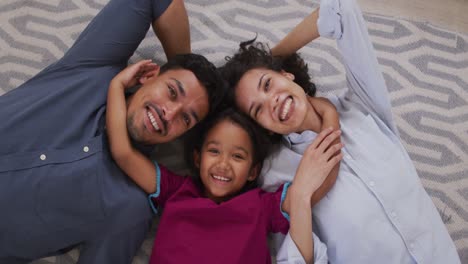 Happy-hispanic-parents-and-daughter-embracing-lying-on-floor-in-living-room