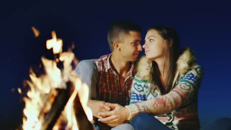 Una-Pareja-Amorosa-Sentada-Junto-Al-Fuego-Cogidos-De-La-Mano-Admirando-El-Fuego