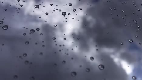 white puffy clouds passing by in the blue sky with sunlight shining through with rain drops on a glass window in focus - hd time-lapse