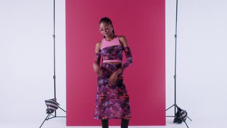 stylish black woman poses with sunglasses, smiling brightly and moving her arms against a vibrant pink background