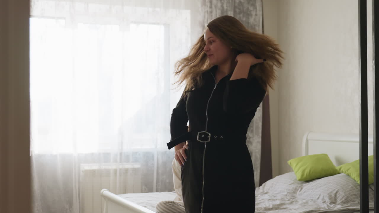 Back view girl enters room, walks toward light then turns to show black dress as friend on bed admires style, indoor bedroom scene, soft morning light, confident step, gentle hair movement