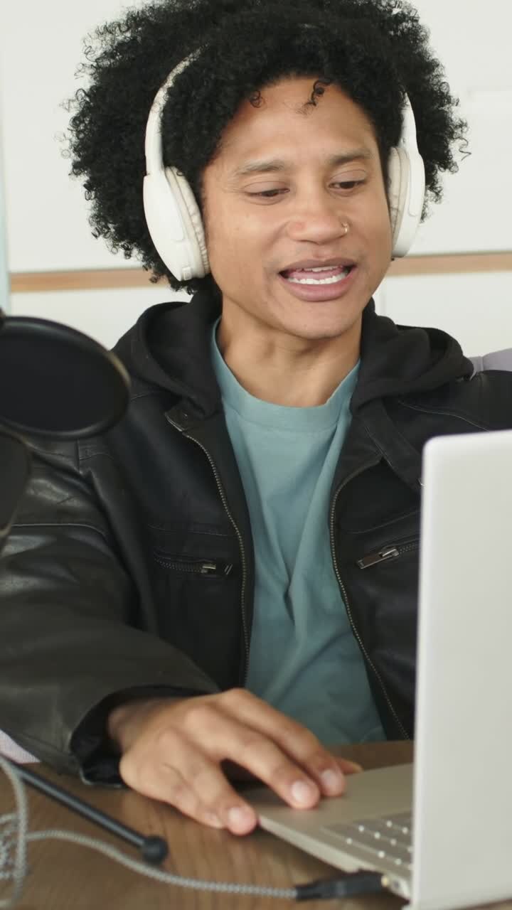 Vertical video: Checking laptop, host listening to audio, recording at desk with mic and phones
