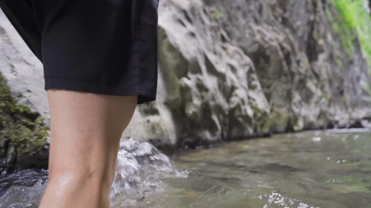 Close-up of man's feet walking in the creek.