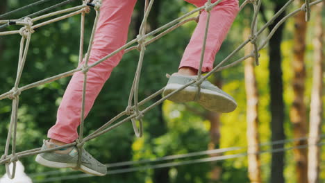 pies de un niño afroamericano caminando por un cable estirado entre árboles