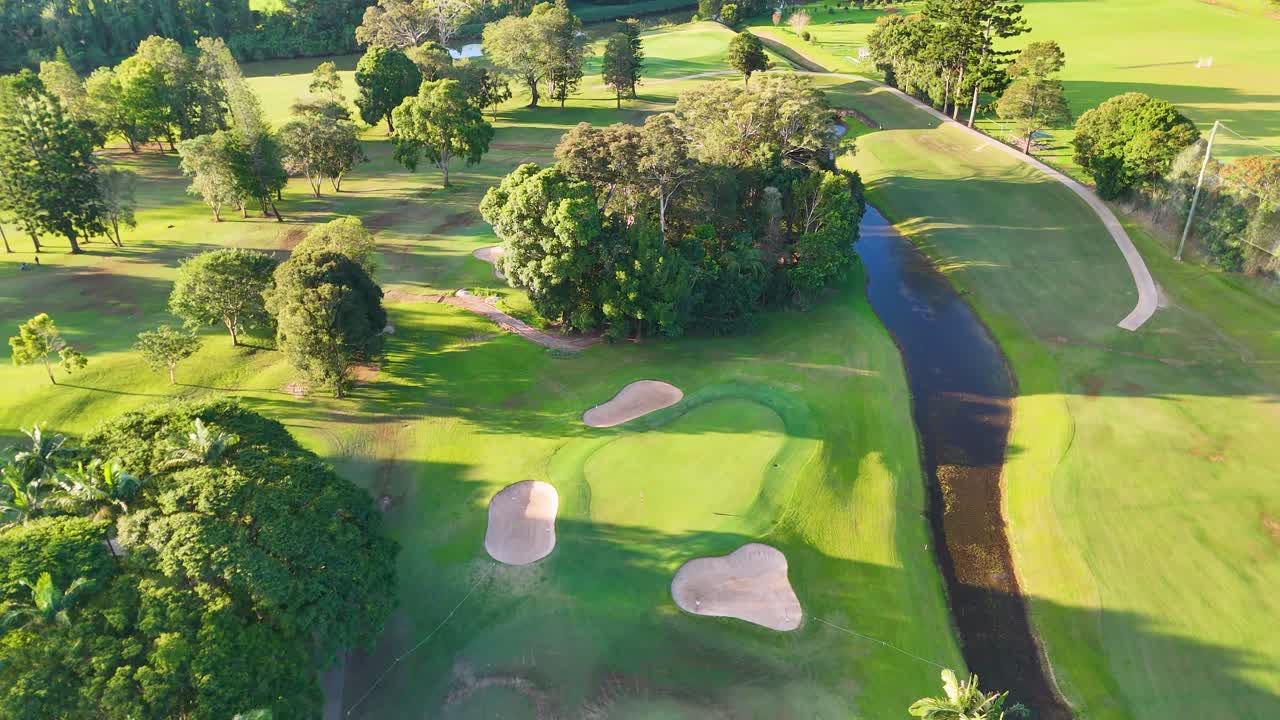 Drone captures lush golf course with fairways, bunkers, and greenery in bright sunlight