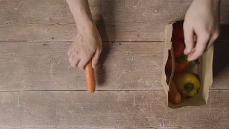 overhead shot of person taking fresh vegetables from paper bag and putting them on wooden surface