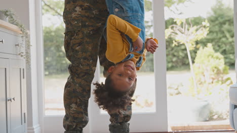 Cerca-Del-Amoroso-Padre-Del-Ejército-En-Casa-Uniforme-De-Licencia-Sosteniendo-A-Su-Hija-Boca-Abajo