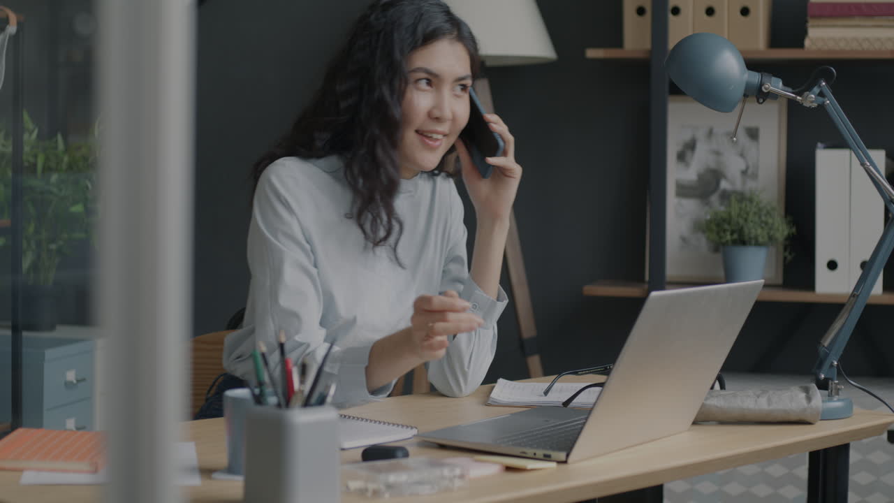 Donna che lavora al laptop e parla al telefono in un ufficio moderno