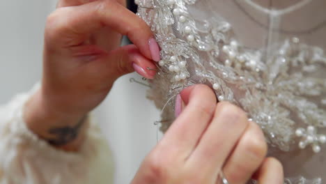 close-up fashion designer for brides in his studio pins needles lace wedding dress. seamstress creates an exclusive wedding dress. secure with pins and needles outline. small private business. sew rhinestones and crystals to the dress thread and needle. jewelry work.