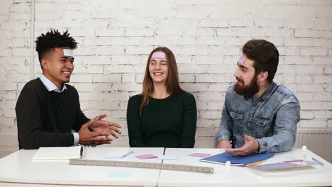 Young-people-pasted-pieces-of-paper-on-forehead-and-guess-words.-Company-of-friends-having-fun-in-the-office.-Diverse-business