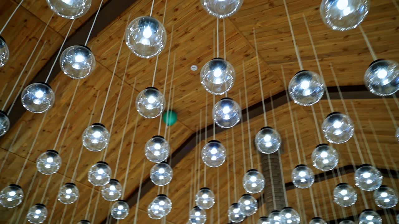 Lamps hanging on celling. Wood background. Warm light. Modern design. Transparent round glass celling lamps. Wooden celling. Modern design. Video from below.