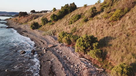 Drone-Pan-Over-Rocky-Beach-and-Along-Coastline-During-Sunset-Golden-Hour