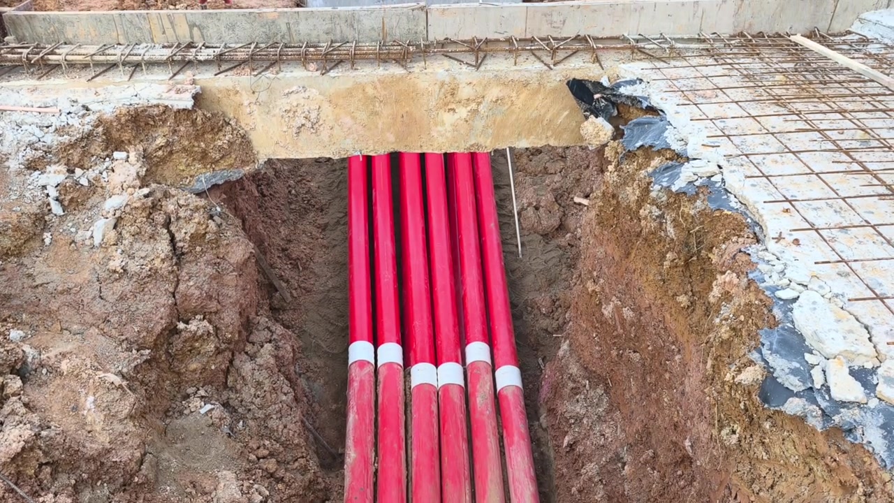 Multiple HDPE pipes are installed inside a ground trench at a construction site. These pipelines will be buried after inspection. They serve as conduits for high voltage electrical cables.